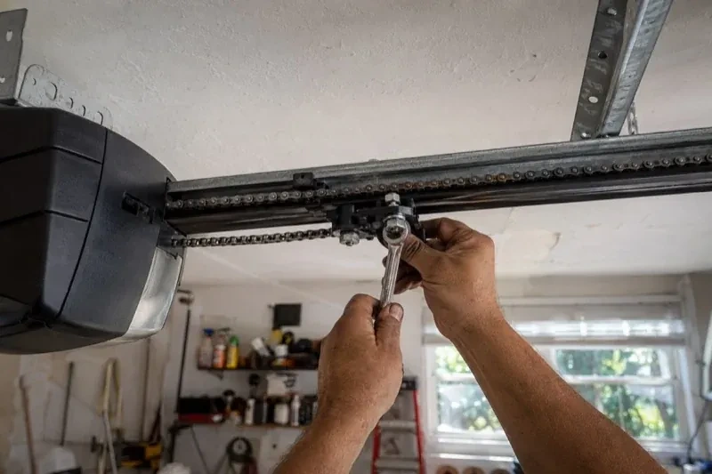 Hands holding a wrench against an opener trolley beneath a chain rail — Chain-Drive Opener Repair, Whitchurch-Stouffville