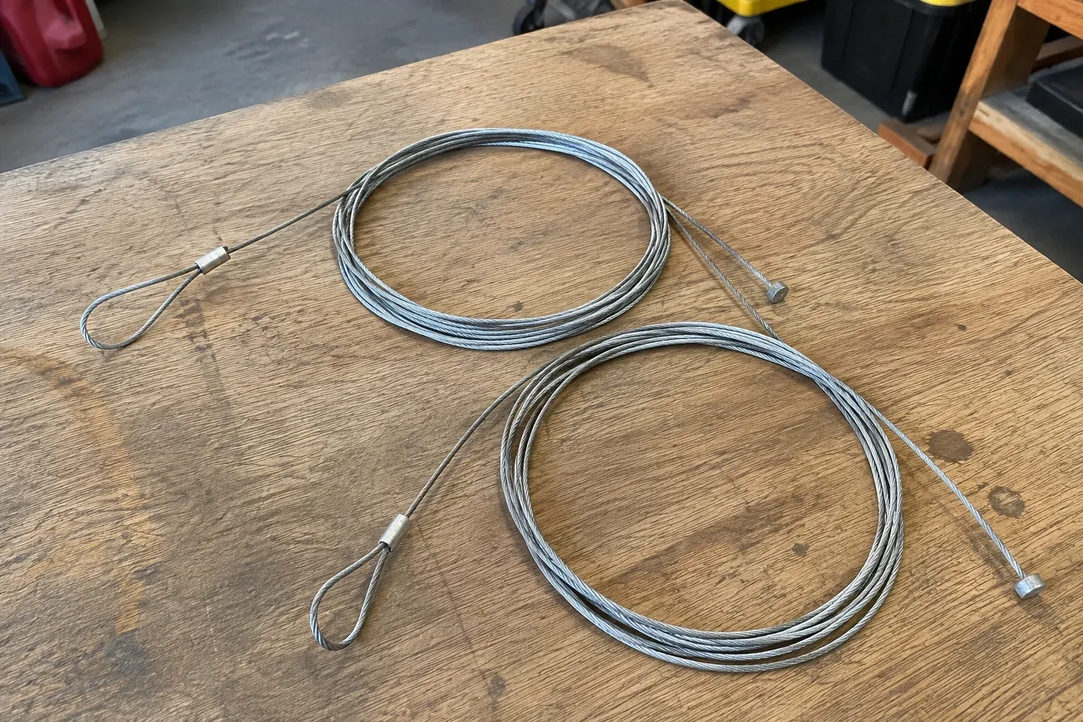 Two coiled steel cables with loop and stop ends on a workbench. — Garage Door Cable Replacement, Whitchurch-Stouffville