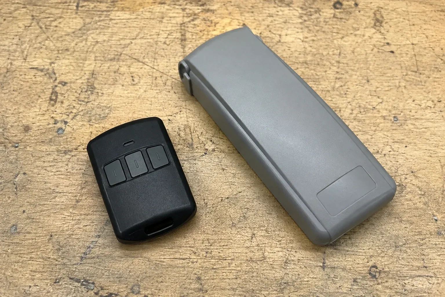 Three-button remote beside a closed grey keypad cover on a workbench. — Garage Door Remote and Keypad Programming, Whitchurch-Stouffville