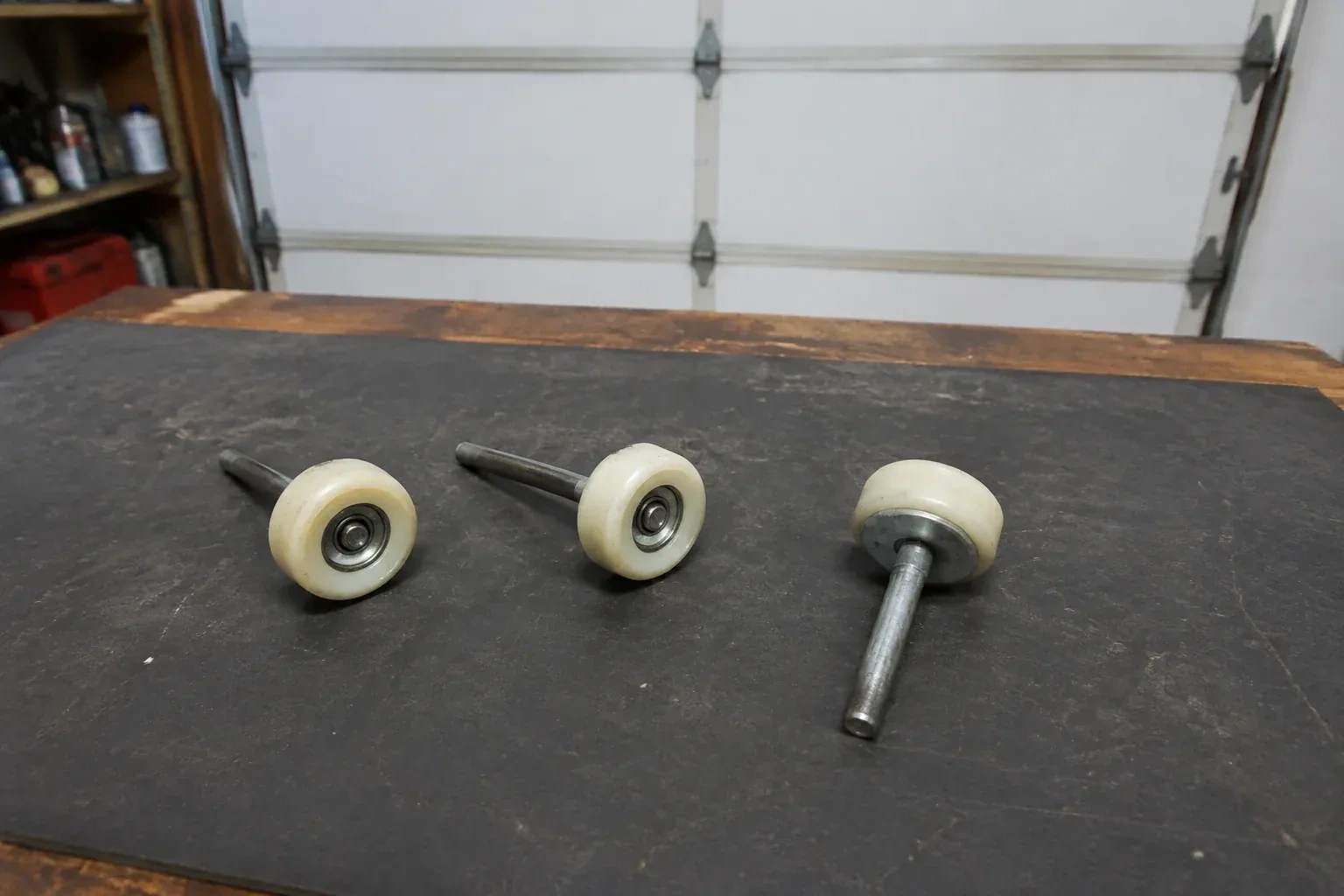 Three detached nylon-wheel garage door rollers with steel stems on a work mat. — Garage Door Roller Replacement, Whitchurch-Stouffville